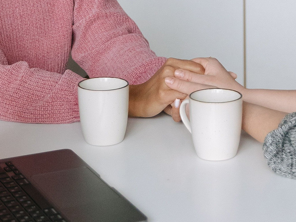 One person comforting another, holding hands across a table