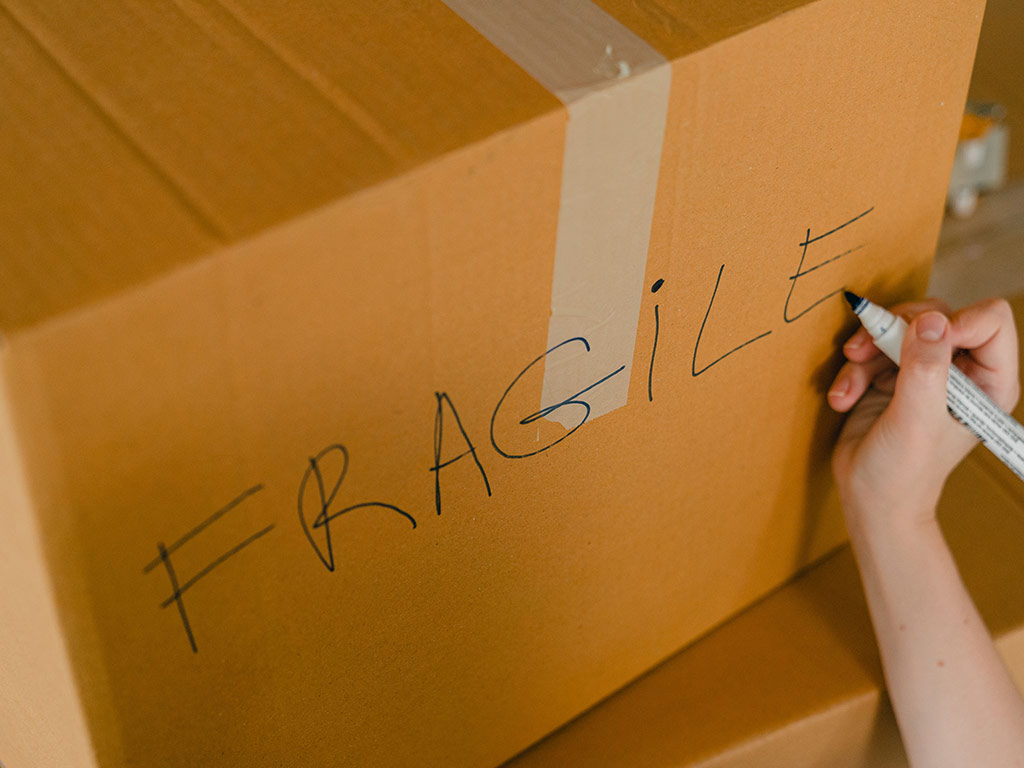 Person writing 'Fragile' on a cardboard box