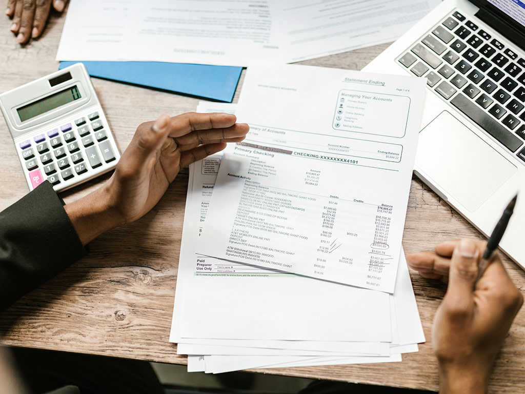 Person reviewing bank statements with a calculator and laptop