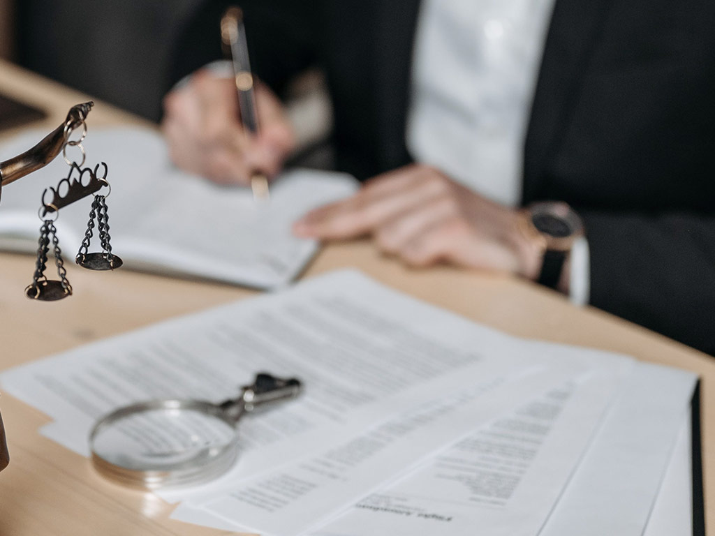 Lawyer making notes beside scales of justice and a magnifying glass