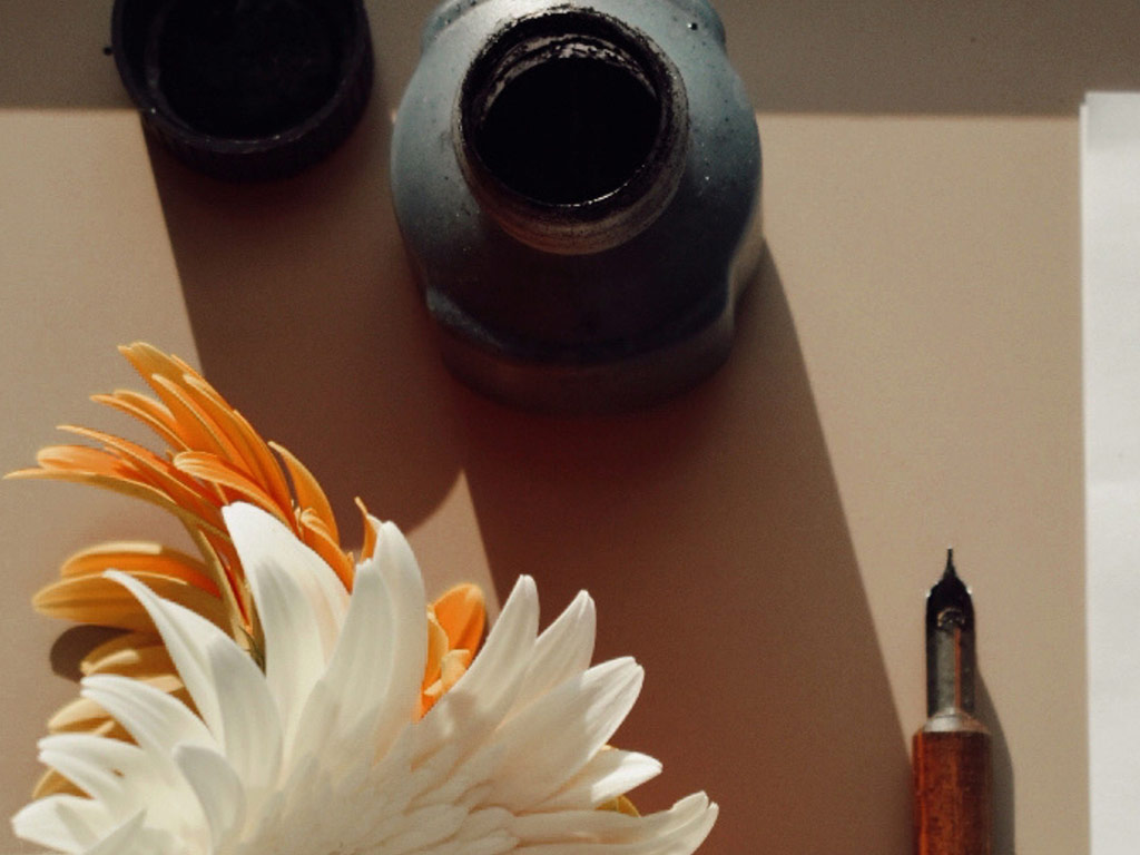 Ink bottle, dip pen and flowers on a desk