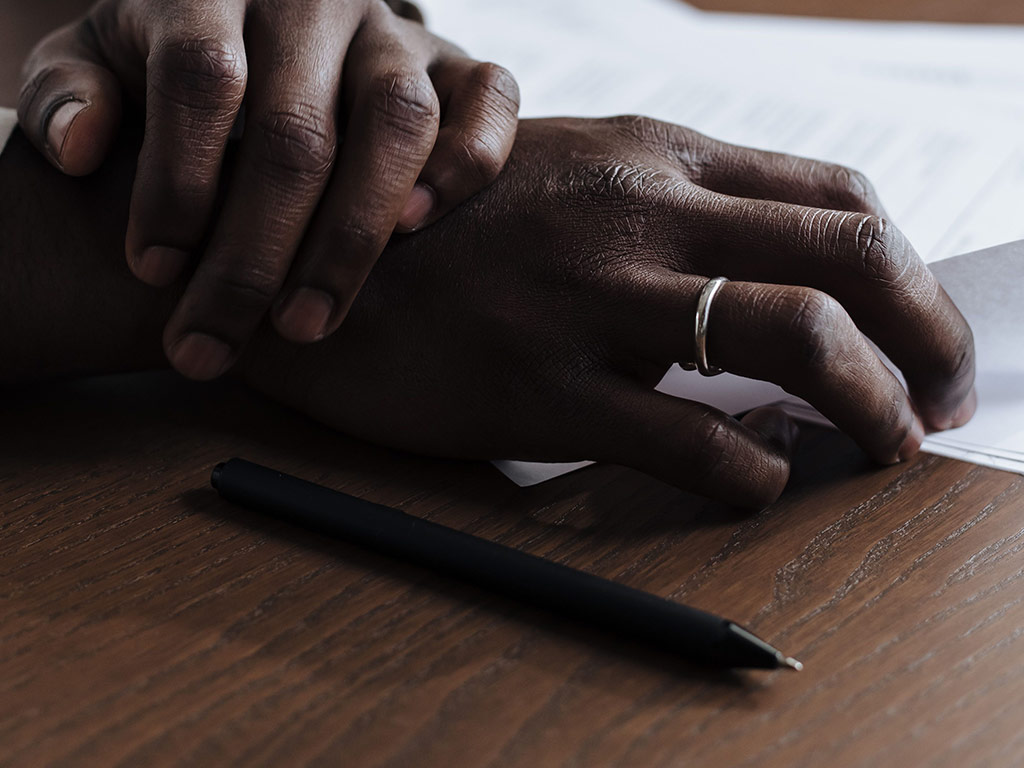 Clasped hands resting on paperwork beside a pen